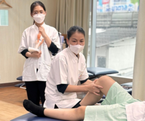 膝関節の模型をもって立つセラピストと、患者役の膝下に手を当てるセラピスト