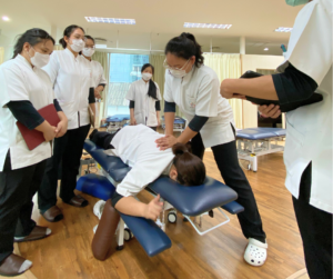 うつ伏せになっている人の背中をマッサージするセラピストとそれを見ているセラピストたち