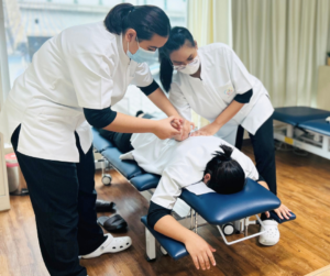うつ伏せになっている人の背中をマッサージするセラピスト　そのセラピストの手をもって指導するもう１人のセラピスト