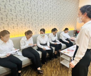 5人がソファに座って手元の資料を読んでいる、１人が立ってそれをみている