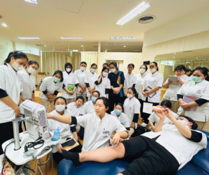 一人のセラピスト膝にエコー検査機を操作してプローブを患者役のスタッフの膝にあてている。それを見ている大勢のセラピストたち。