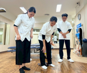 ３人のセラピストが立っている。一人は自分の膝を指さしている