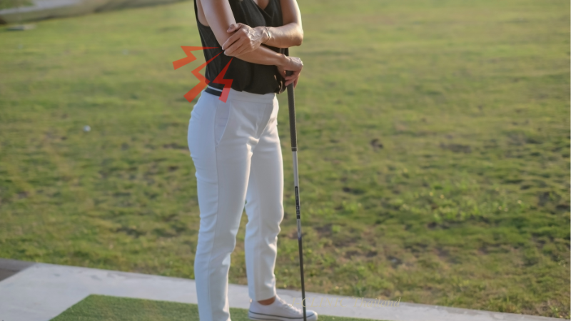 肘を痛そうに抑えているゴルファー