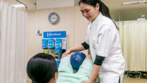 患者様が仰向けになって膝をたてている、膝の間に柔らかいボールを挟んで、頭をあげようとしている。それをセラピストがサポートしている