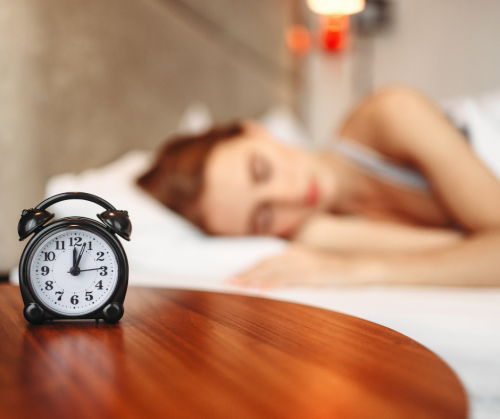 ベッドサイドに時計を置いて寝ている女性