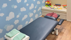 空の色と雲のイラストが描かれた壁紙の部屋にベッド、おもちゃがおいてある