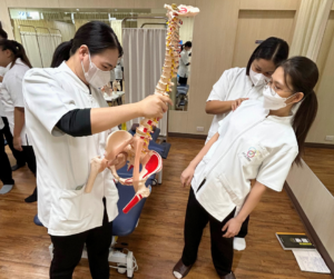 背骨と骨盤の模型をもっているセラピスト、腰を後にそらしているセラピストとそれを支えているセラピスト