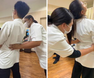 立ってうしろに体を反る人の背中に手を当てるセラピスト