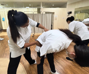 立ったまま前に体を倒す人の腰に後ろから手をあてるセラピスト