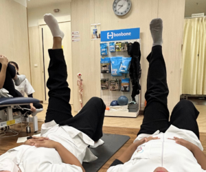 仰向けになって左の足だけをまっすぐ上に伸ばしているセラピスト2人